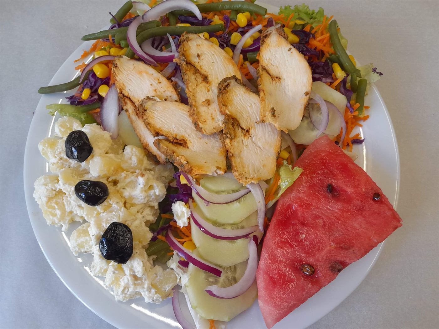 Assiette de poulet grillé, salade composée et tranche de pastèque